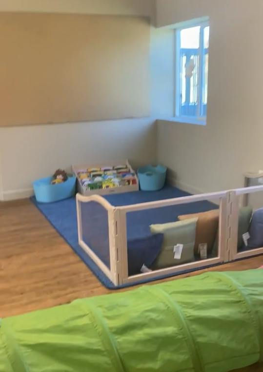 Play area with blue mat, toy storage, and green tunnel