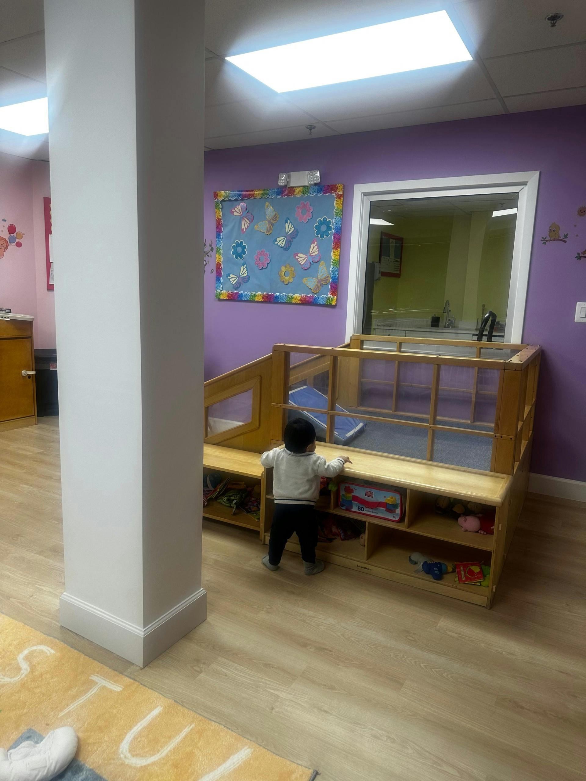 Child standing, looking over a wooden play structure in a colorful room