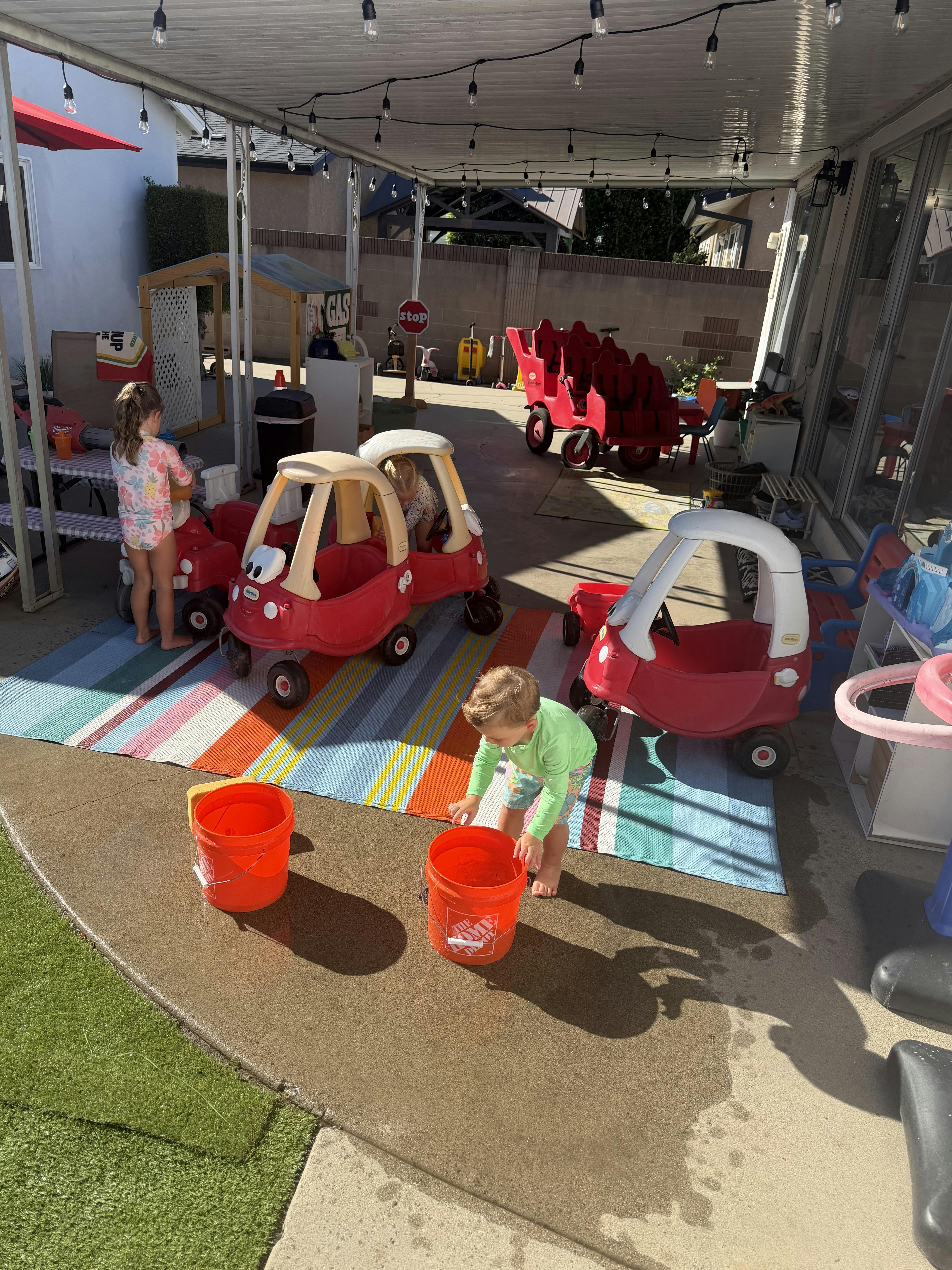 Children playing with toy cars and buckets on a patio