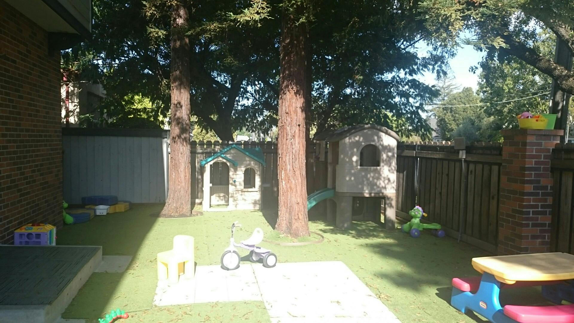 Outdoor play area with artificial grass, trees, and playhouses