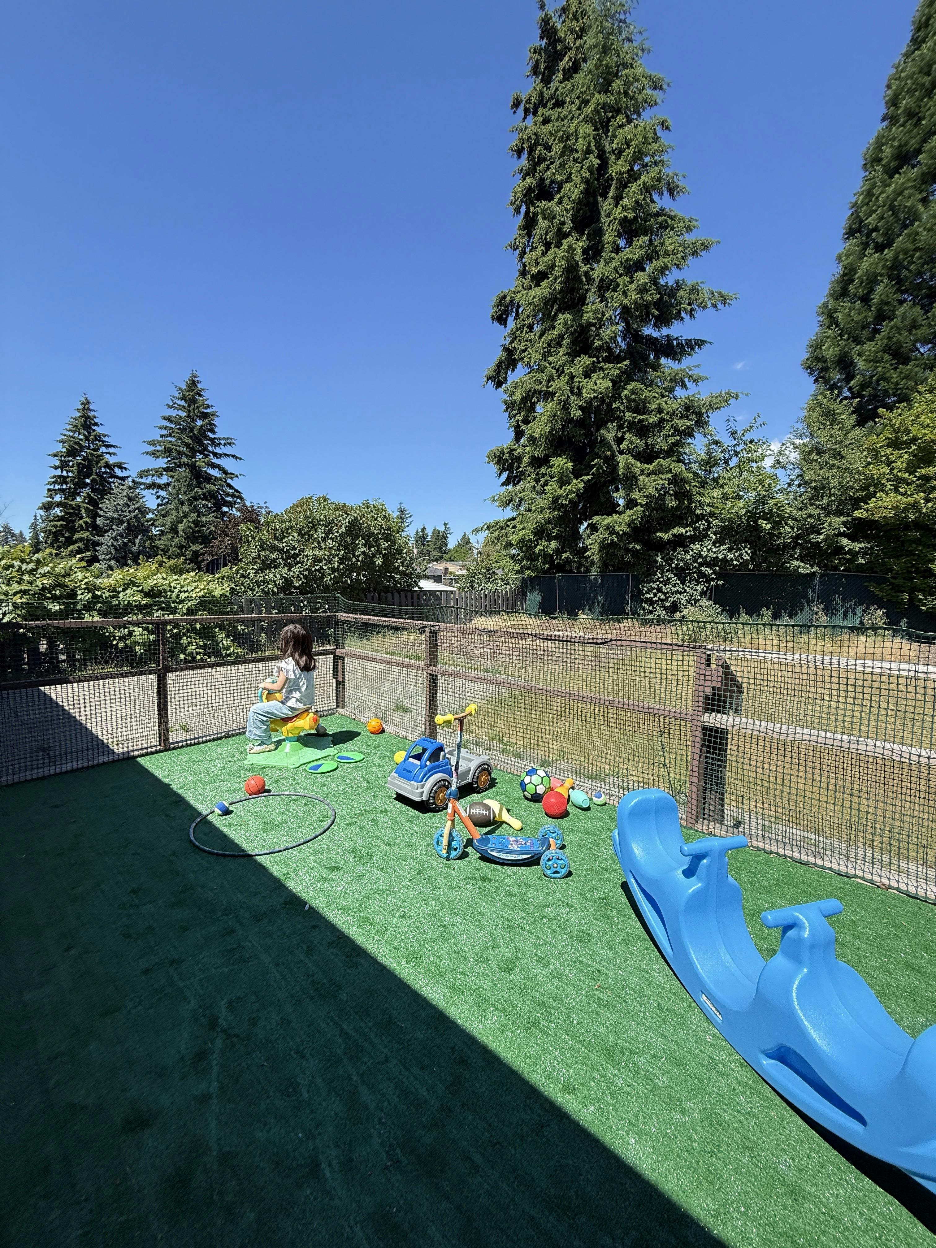 Child sitting on a toy in a fenced outdoor play area