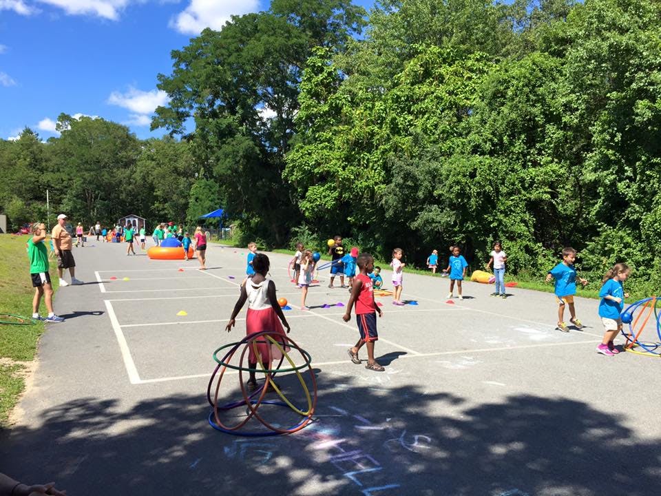 Children playing outdoors on an asphalt surface with trees in the background