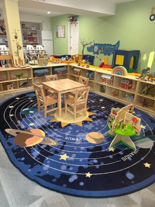 Children's classroom with solar system rug, small table, and shelves of toys