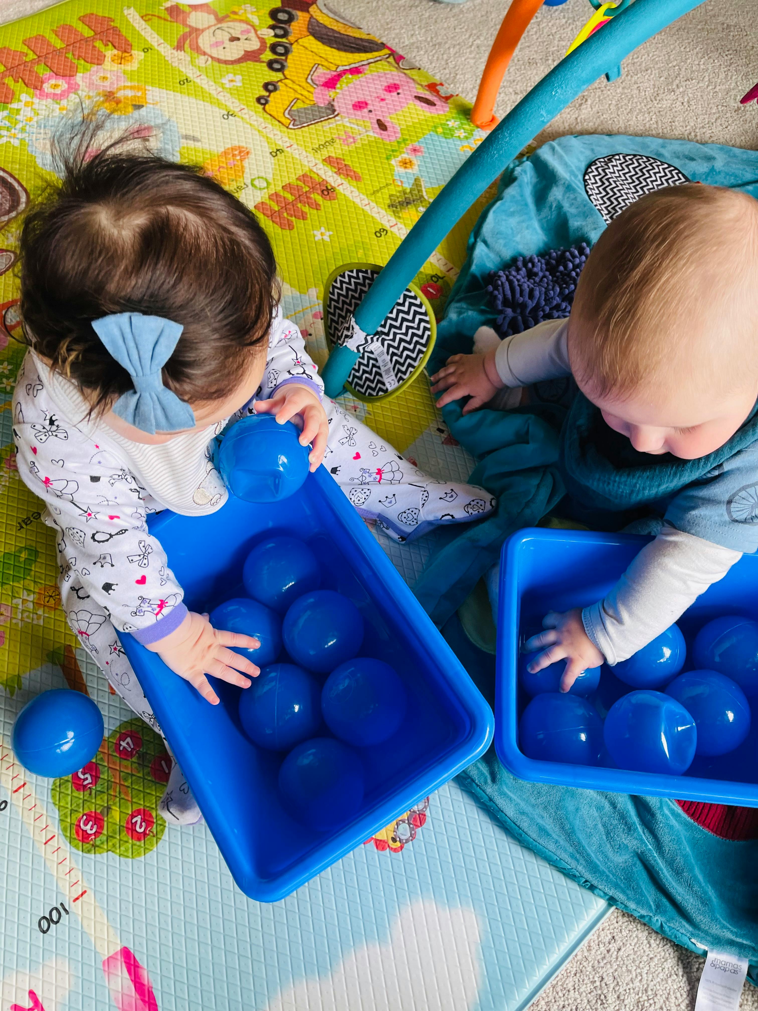 Two children playing with blue balls in plastic bins