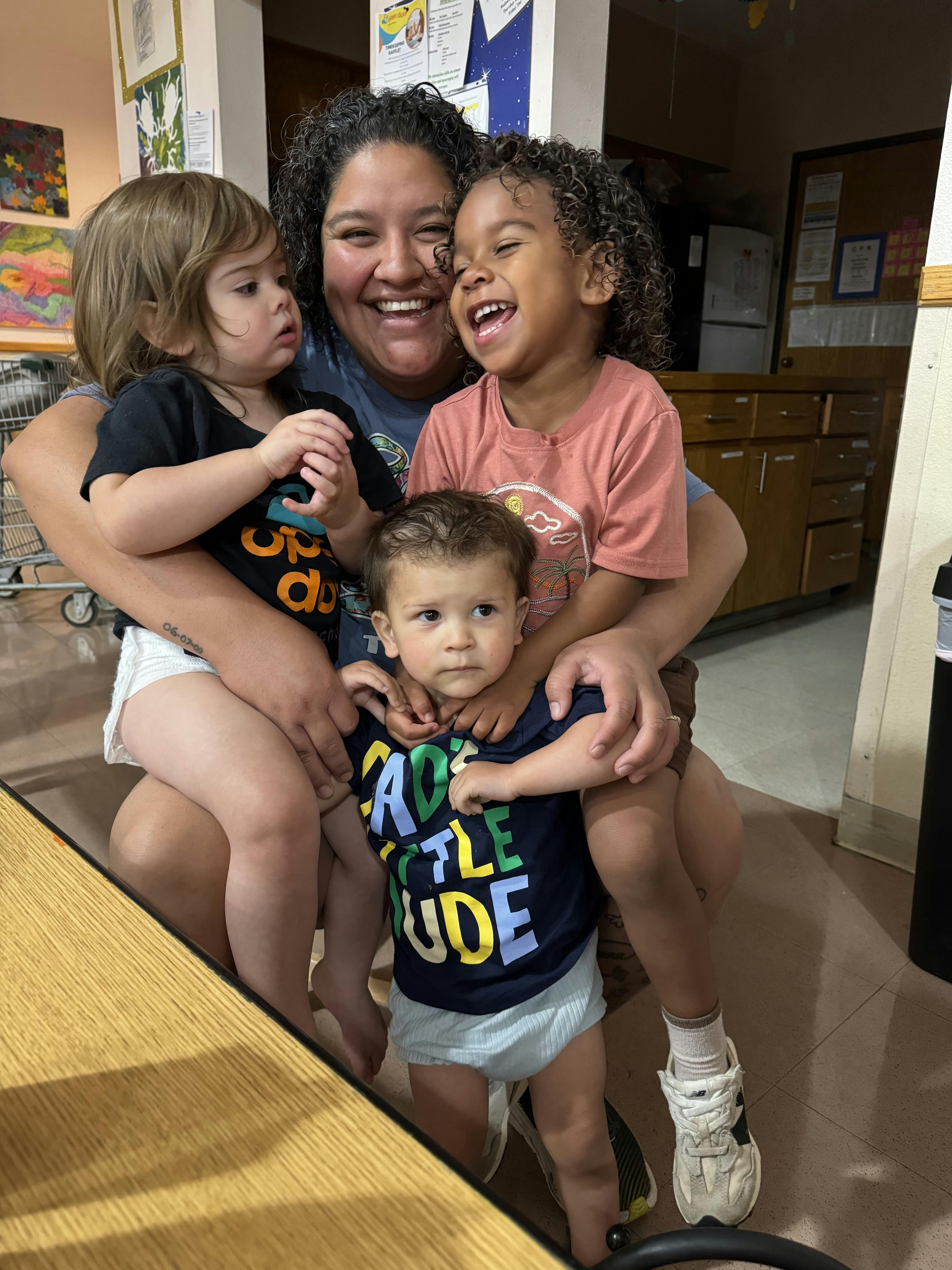 Person holding two children, with a third child standing in front