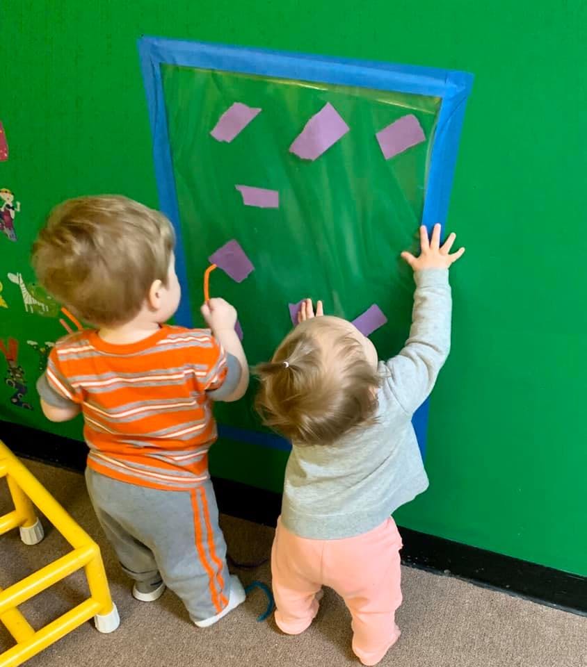 Two children playing with a green sensory board on a wall