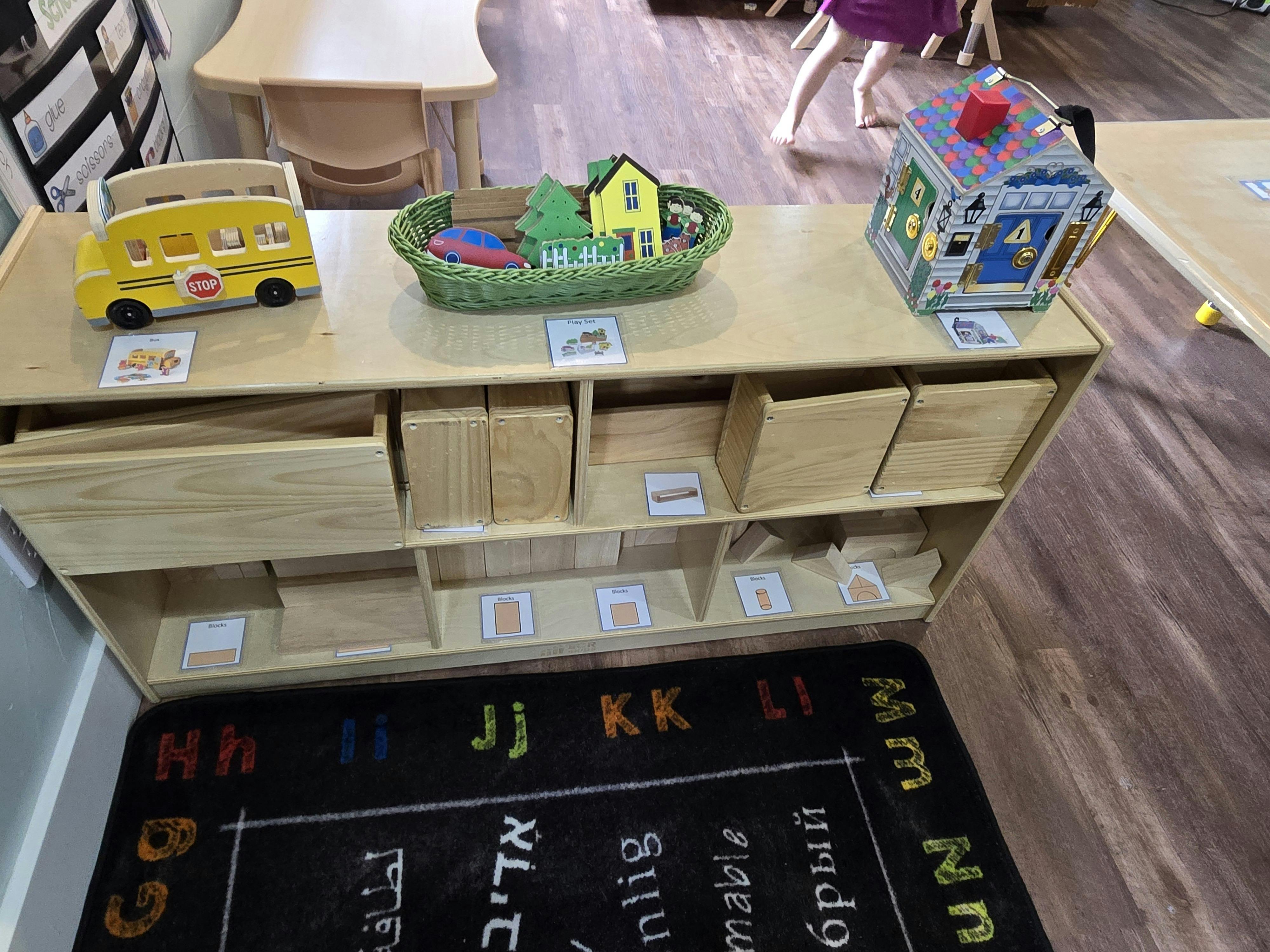 Wooden shelf with a toy school bus, a basket with toy houses, and a toy cube