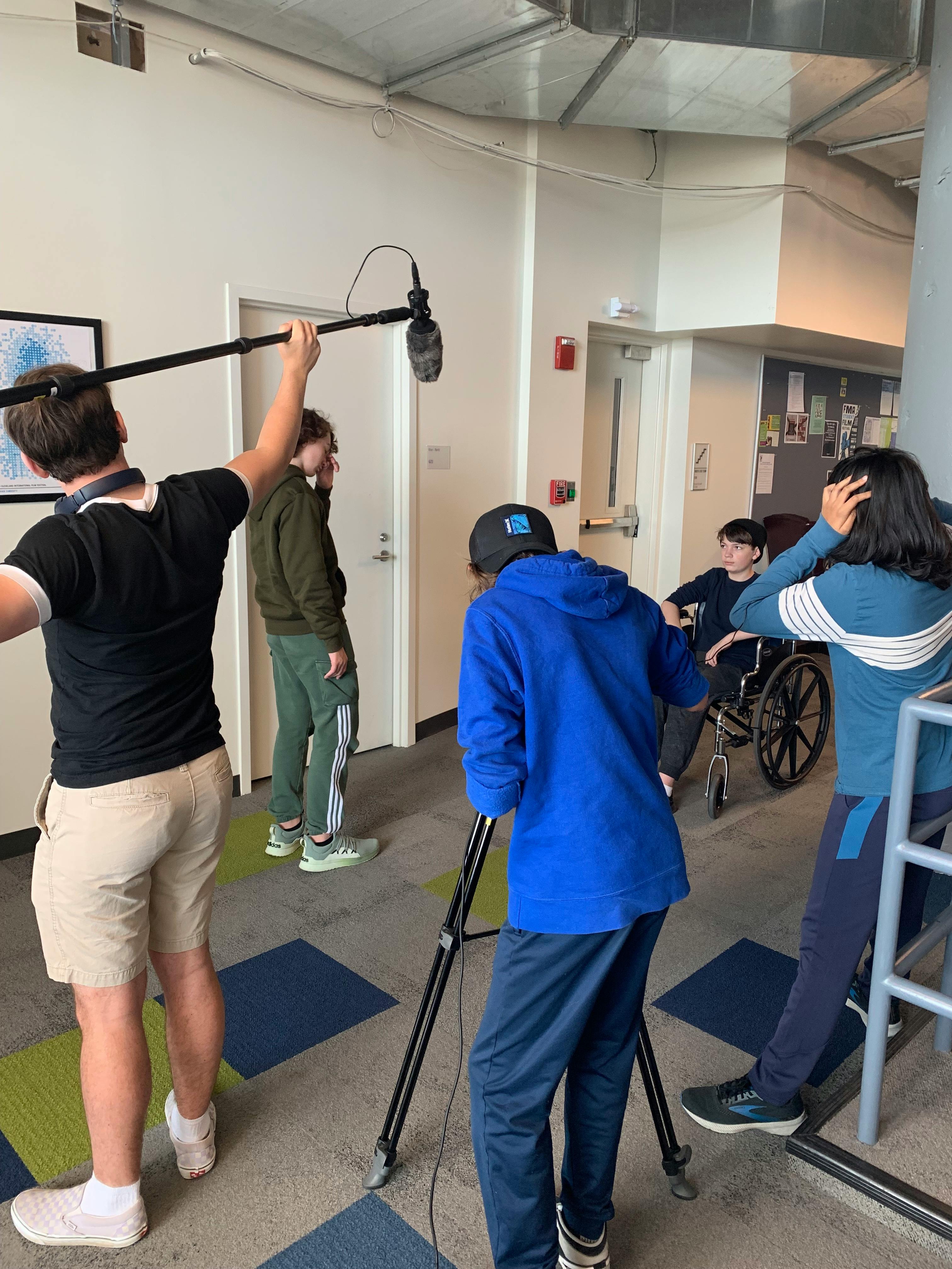 People filming with a boom mic and camera, one person in a wheelchair