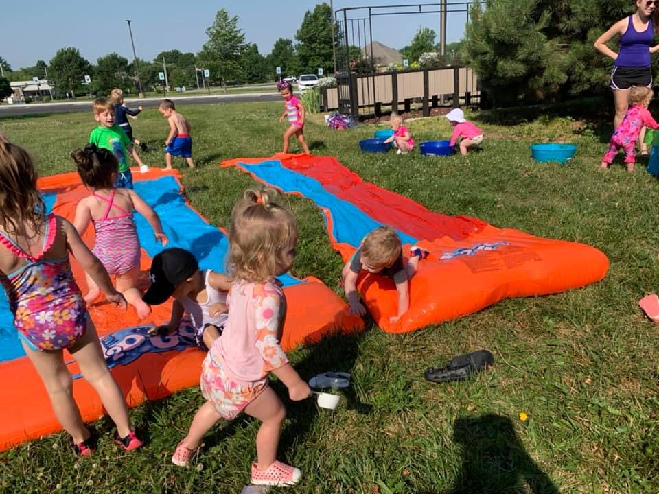Children playing on inflatable water slides in a grassy area
