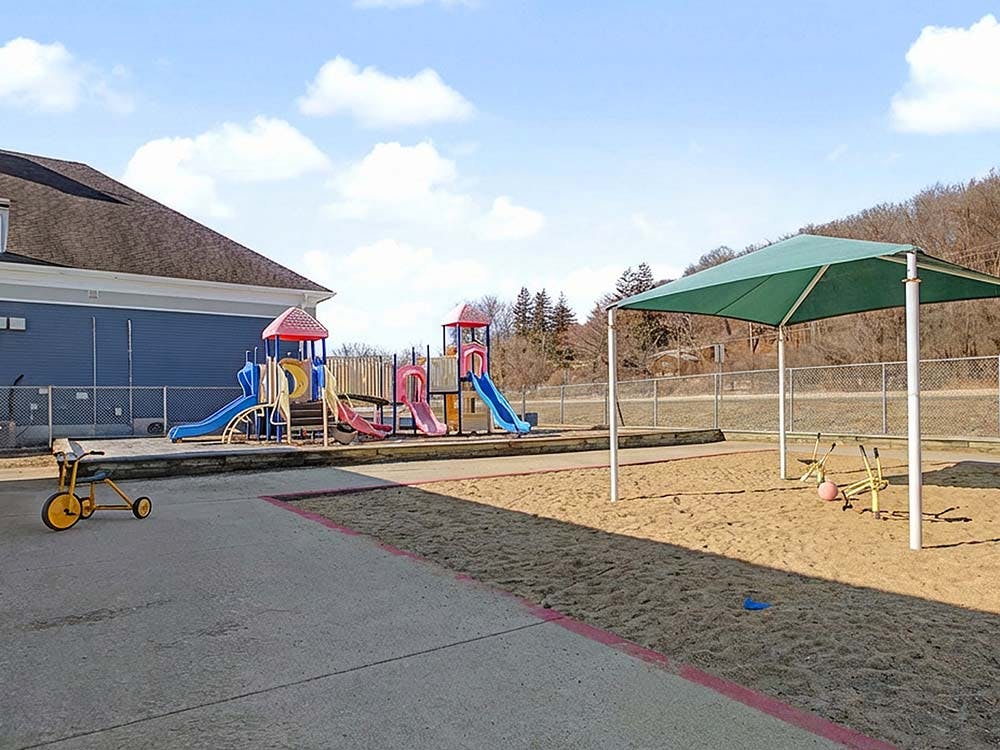 A playground with a blue building, colorful slides, a sandbox, and a green canopy