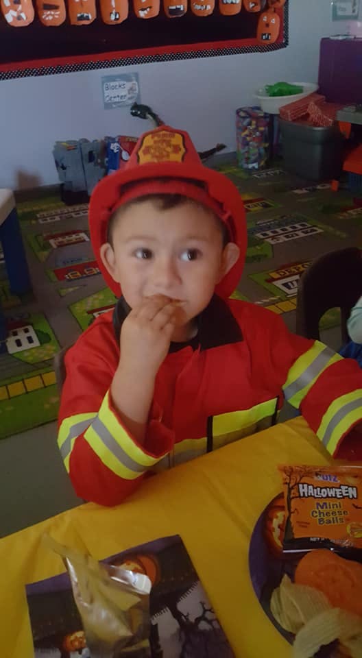 Child in firefighter costume eating a snack at a table