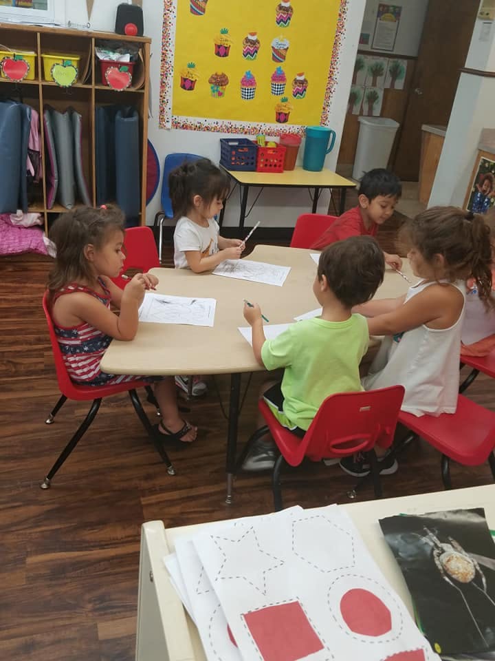 Four children sitting at a table doing schoolwork in a classroom