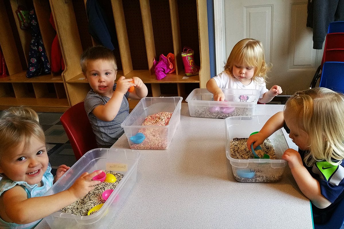 Four children playing with sensory bins at a table