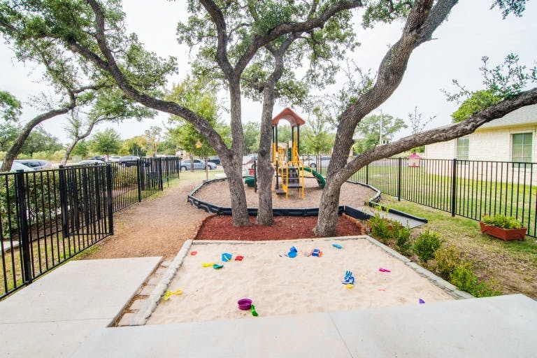 Outdoor playground with sandbox, play structure, and trees