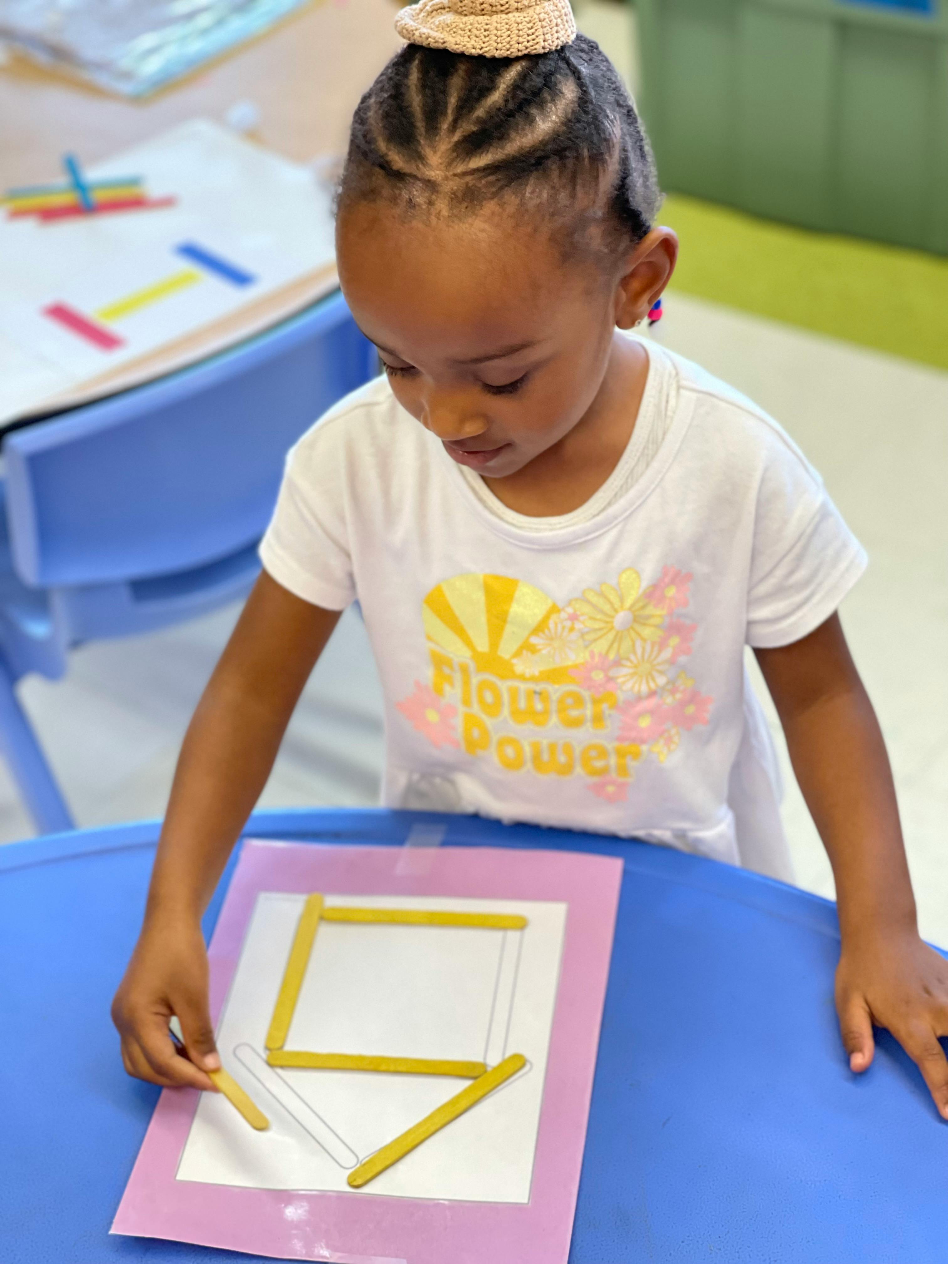 Child arranging craft sticks on a paper template