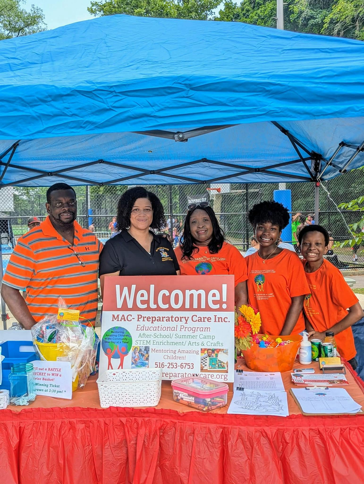 Five people standing behind a table with a "Welcome!" sign