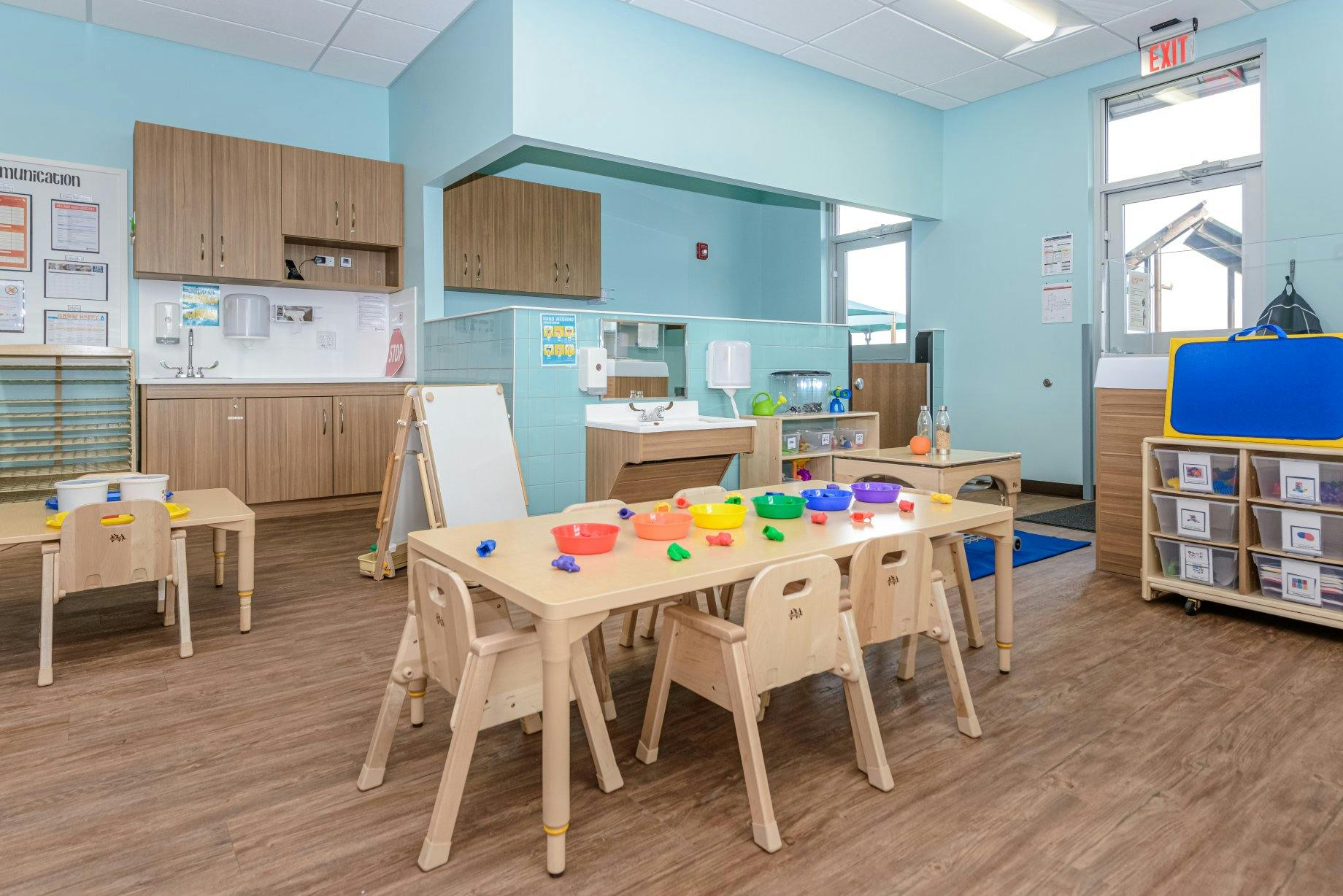 Classroom with child-sized tables and chairs, wood cabinets, and two sinks