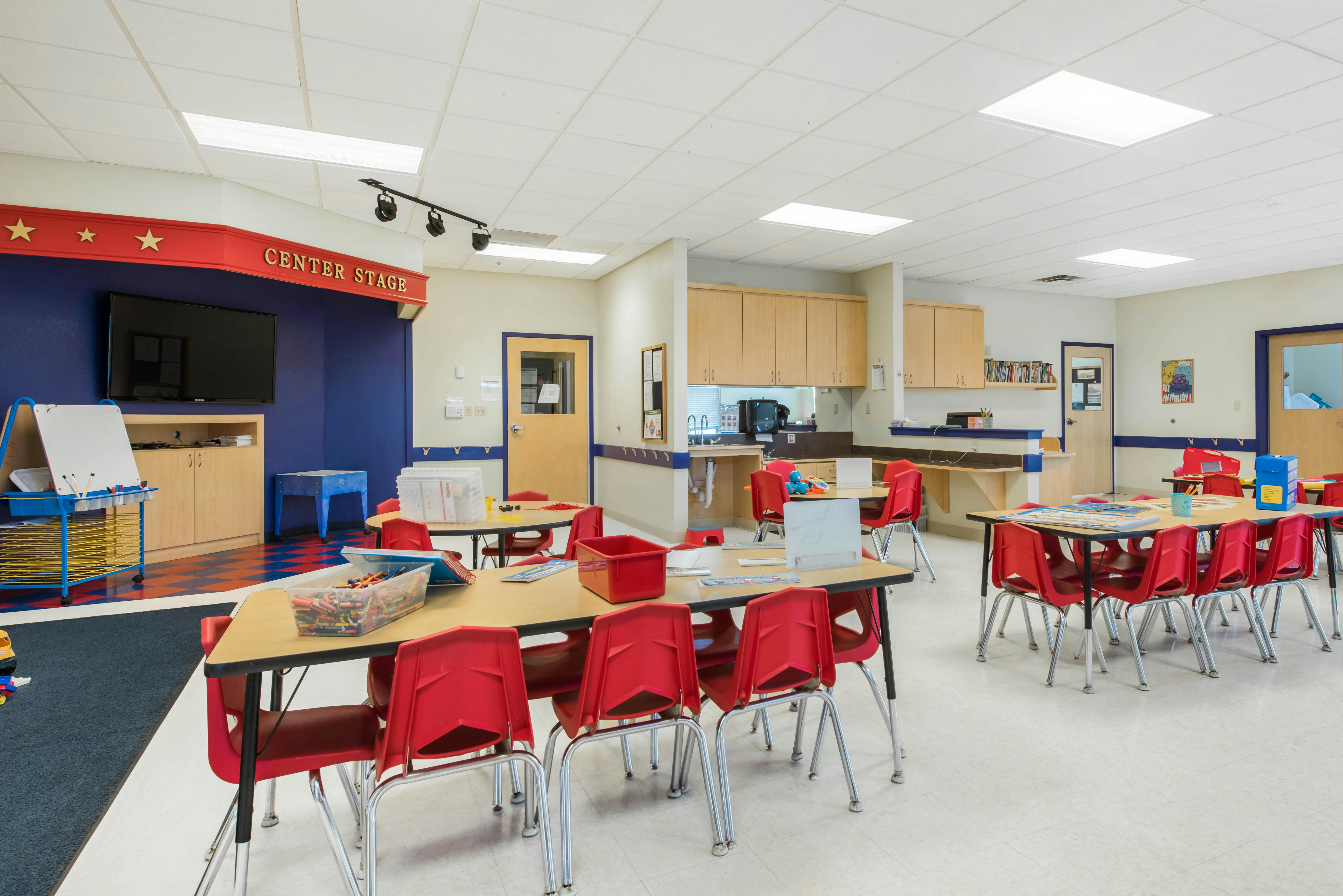 Classroom with small tables and red chairs, one area labeled "CENTER STAGE"