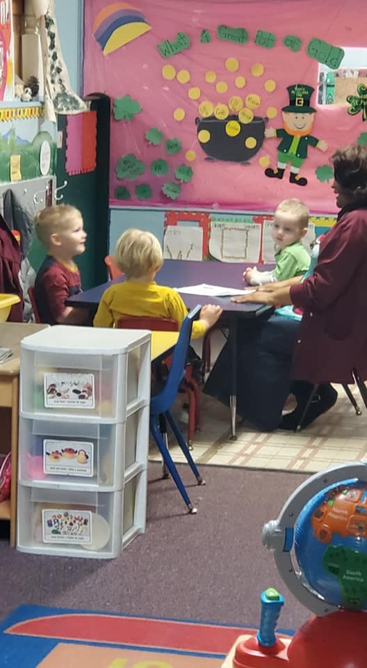 Adult and three children sitting at a table in a classroom