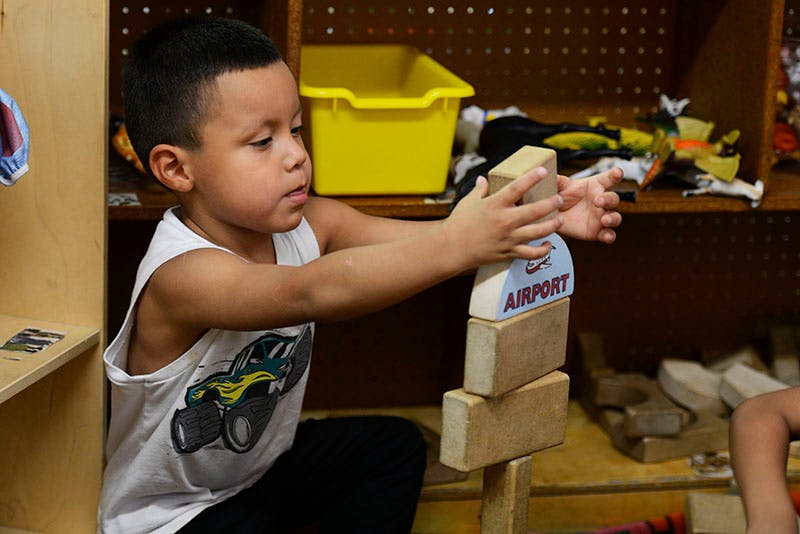 Child stacking wooden blocks with one block labeled "AIRPORT"