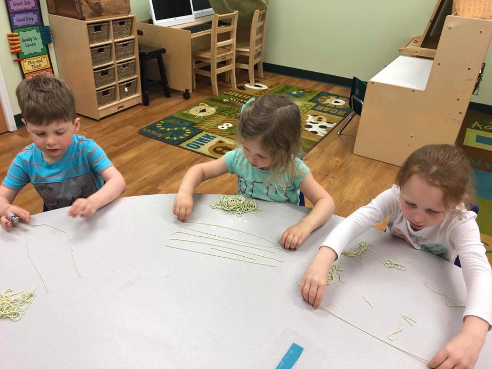 Three children at a table playing with string
