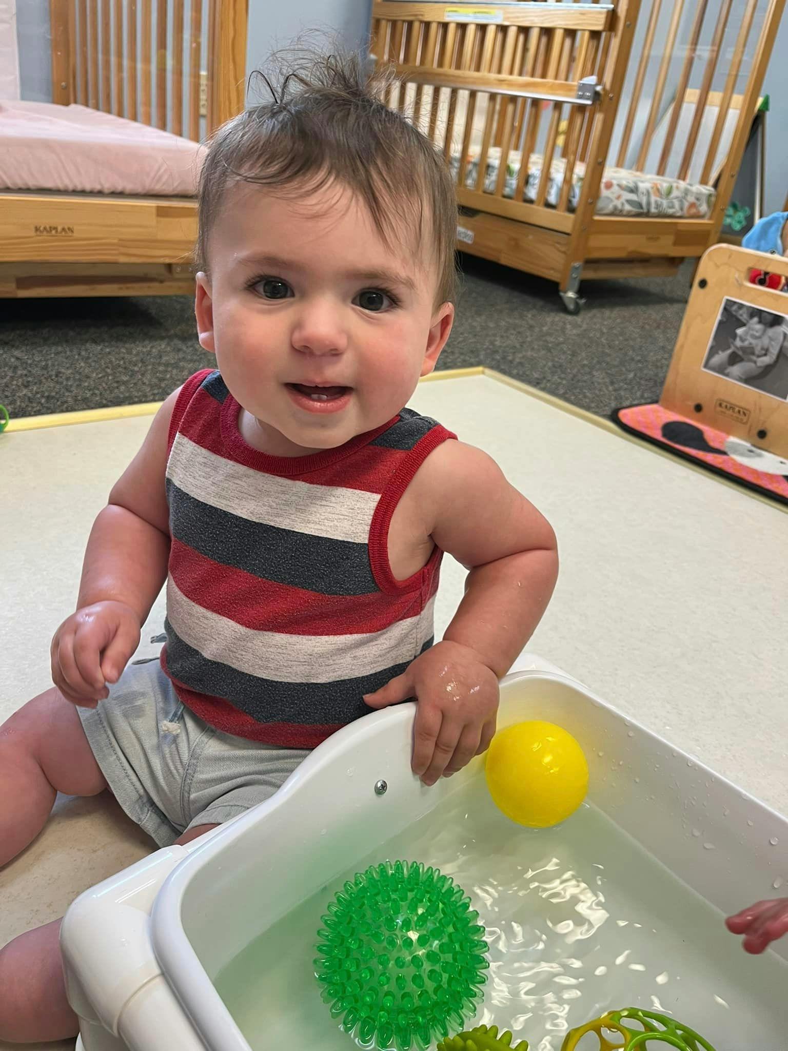 Child sitting next to a tub of water with toys