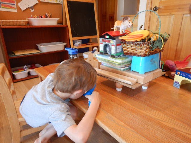 Child looking through a blue toy at a table