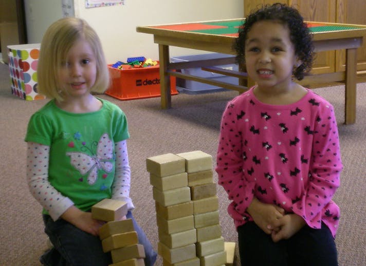 Two children kneeling next to a stack of wooden blocks