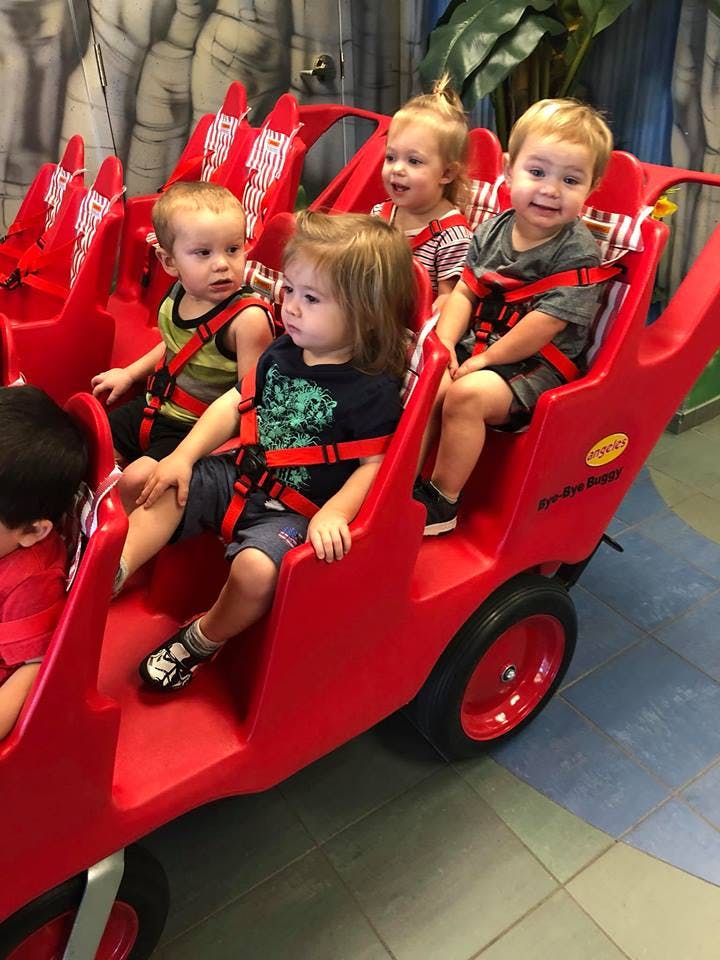 Multiple children seated in a red multi-seat stroller