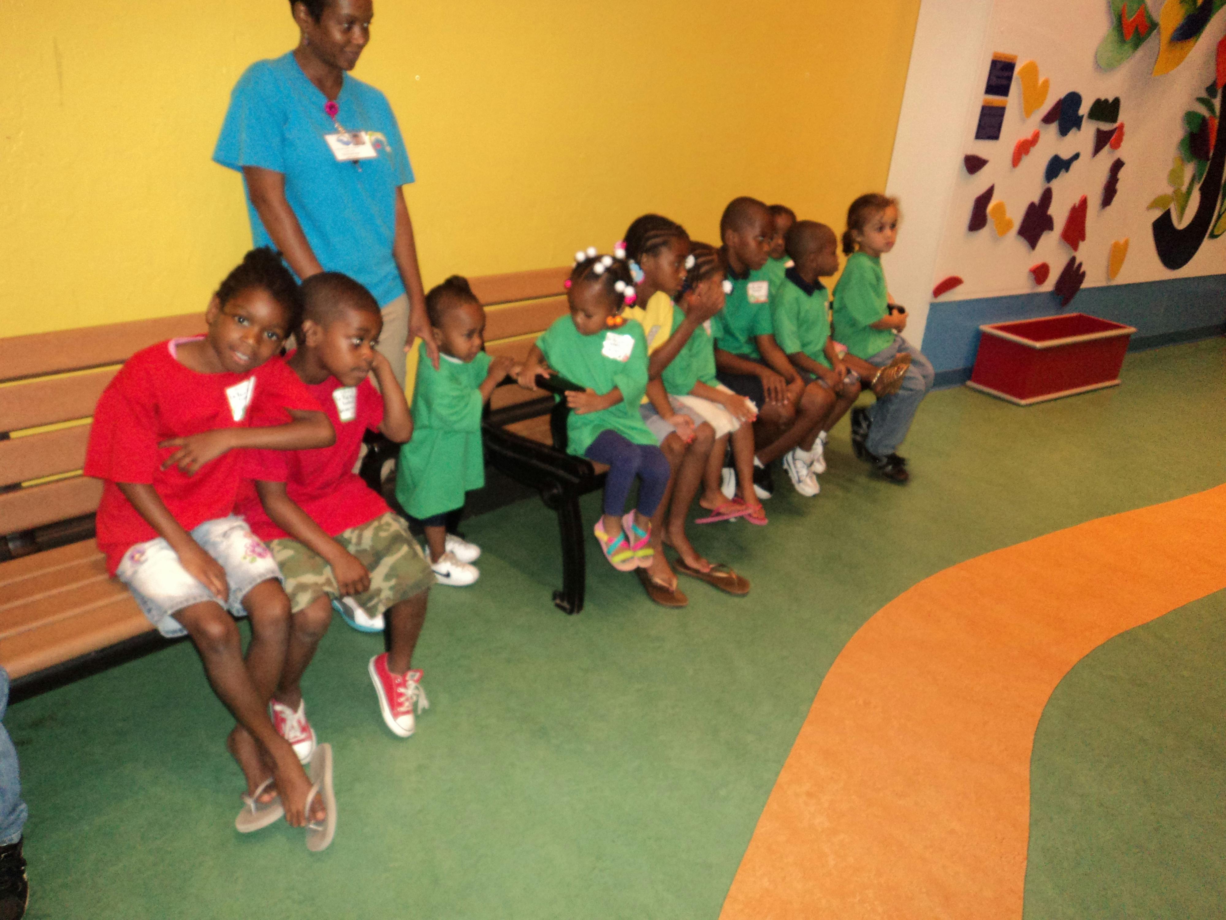 Adult and group of children sitting on benches in a room