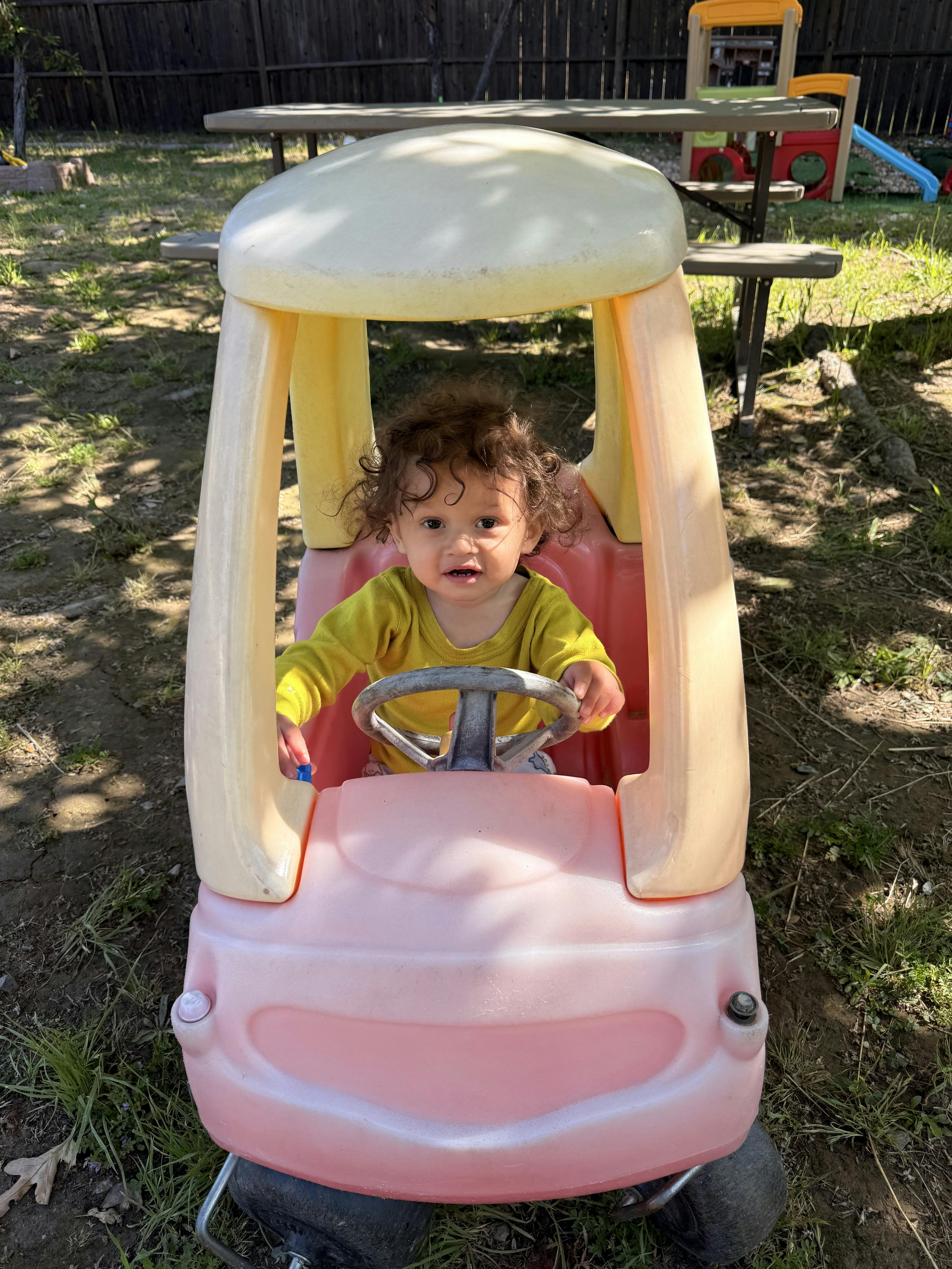 Child with curly hair in a toy car outdoors