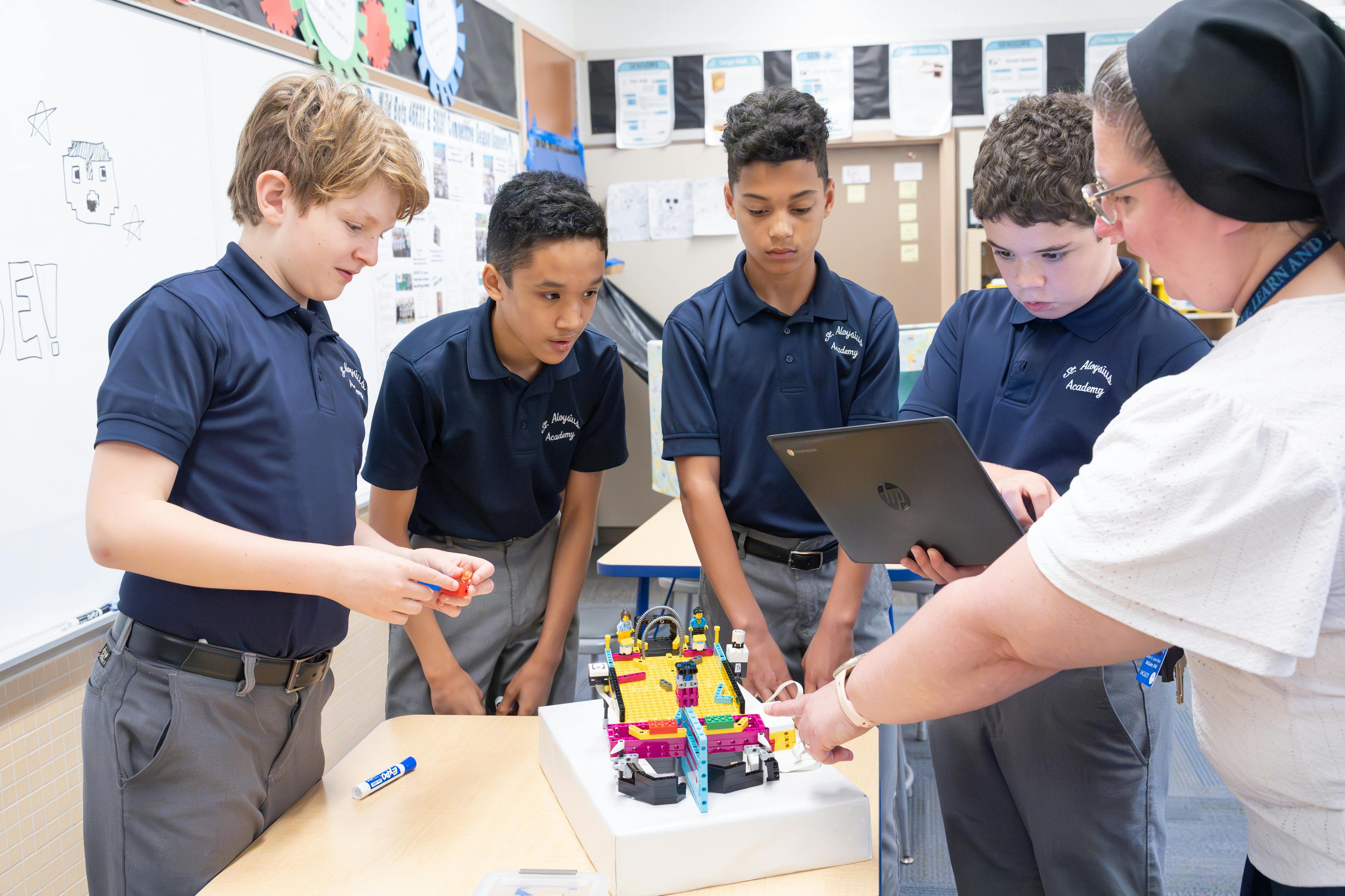 Adult and four teens in a classroom looking at a robot and tablet