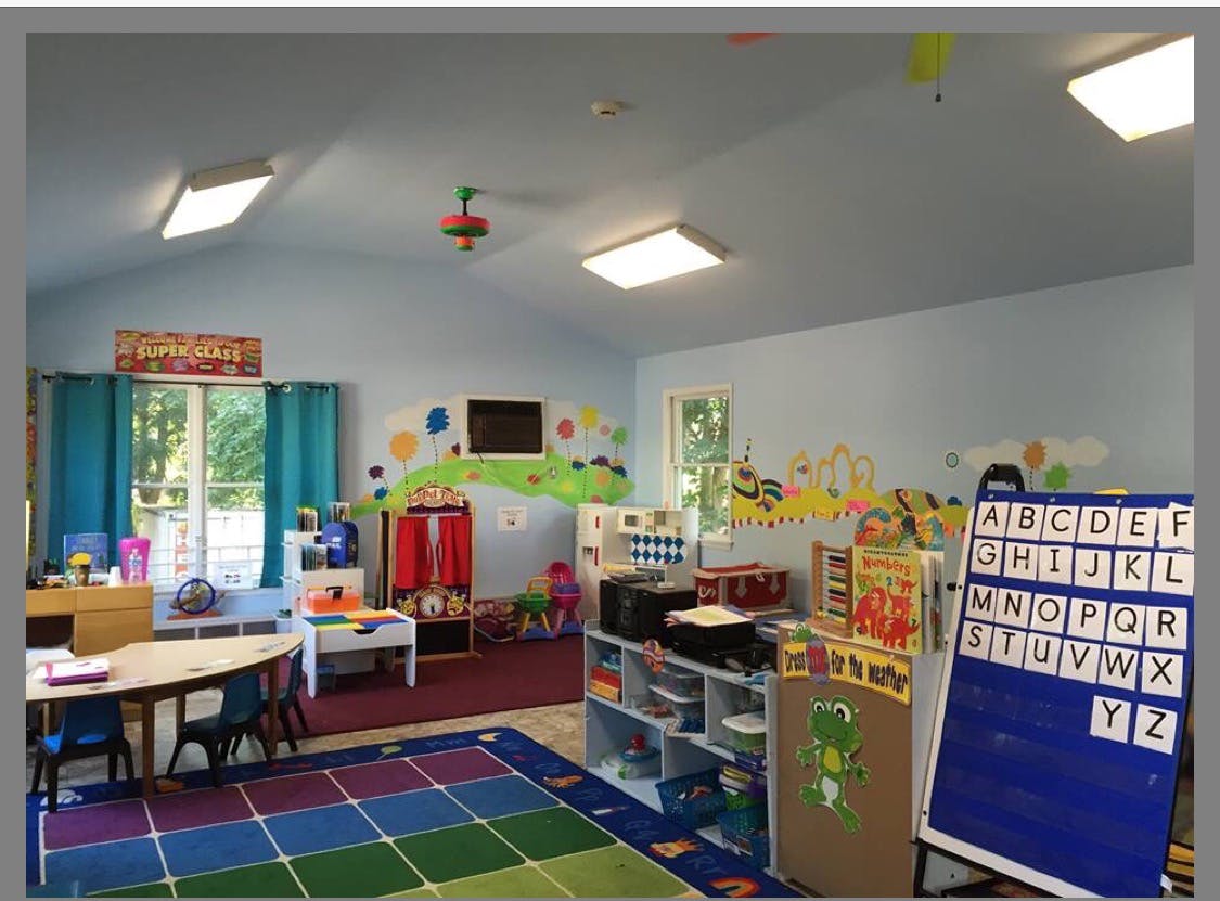 A colorful classroom with a rug, tables, shelves, and an alphabet board