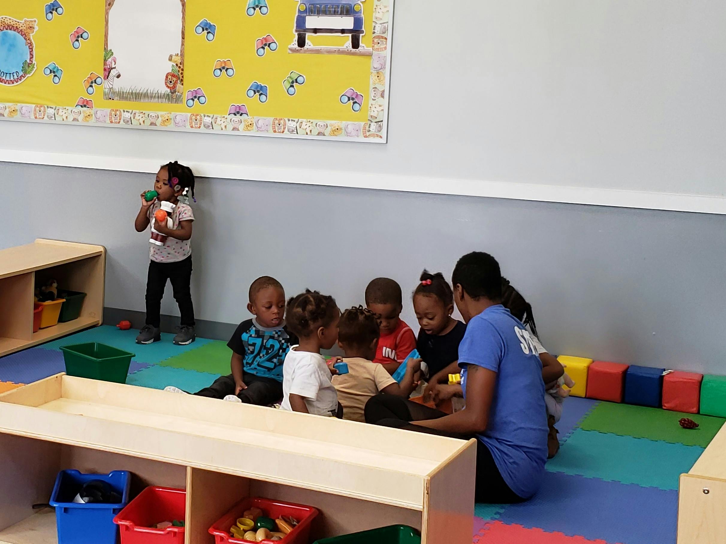 Adult and children sitting on floor in classroom, one child standing
