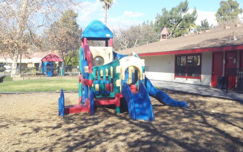 Colorful playground structure with slides on wood chips next to a building