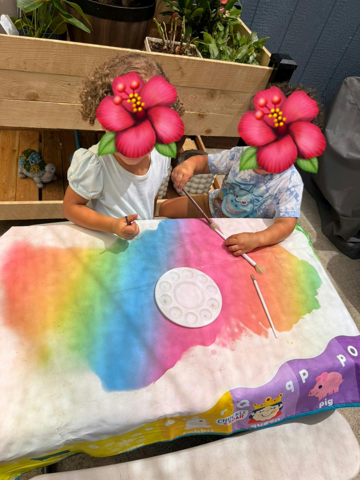 Two children painting on a colorful activity mat at a small table