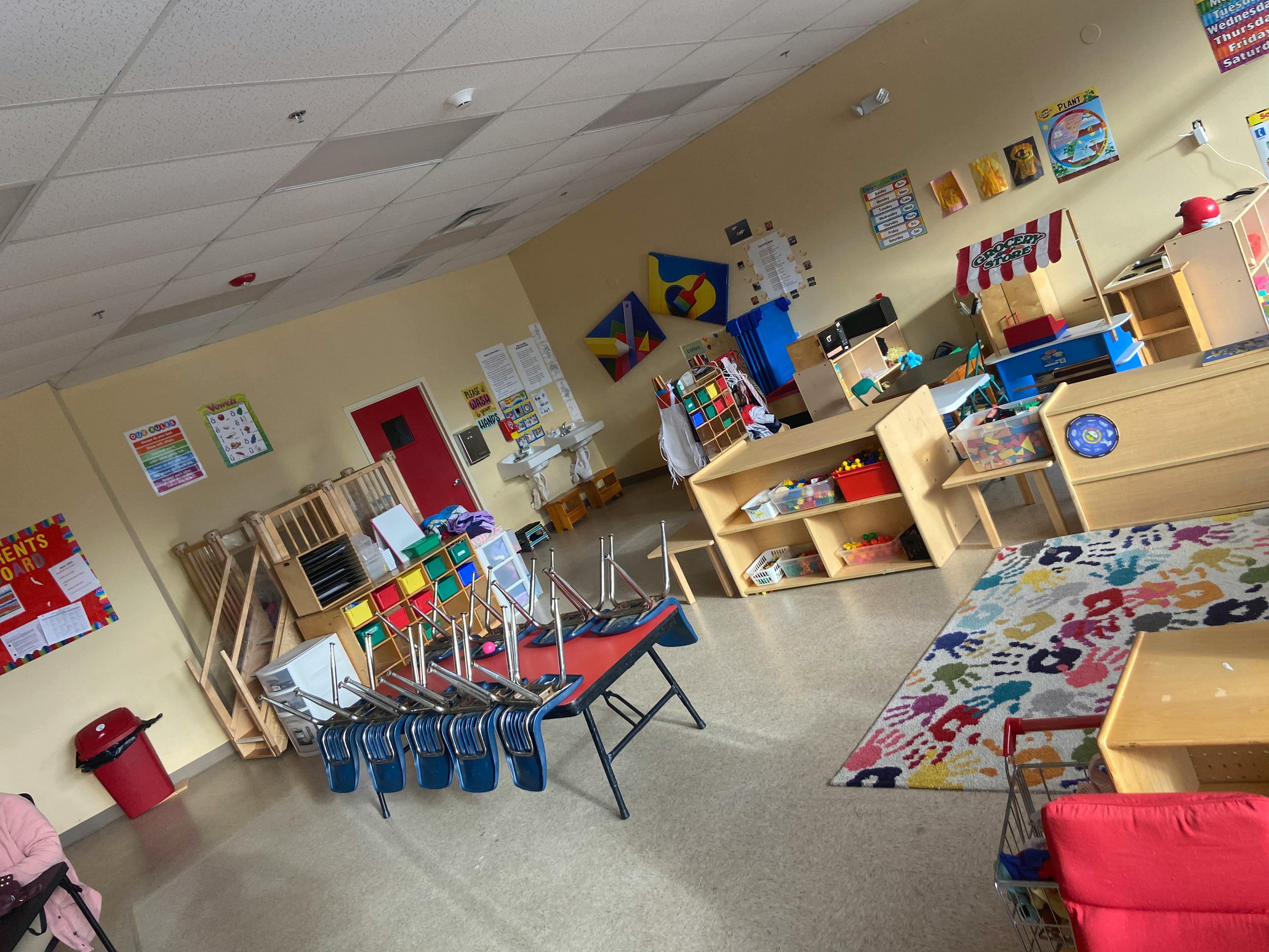 Classroom with tables and chairs, shelves, and a colorful rug