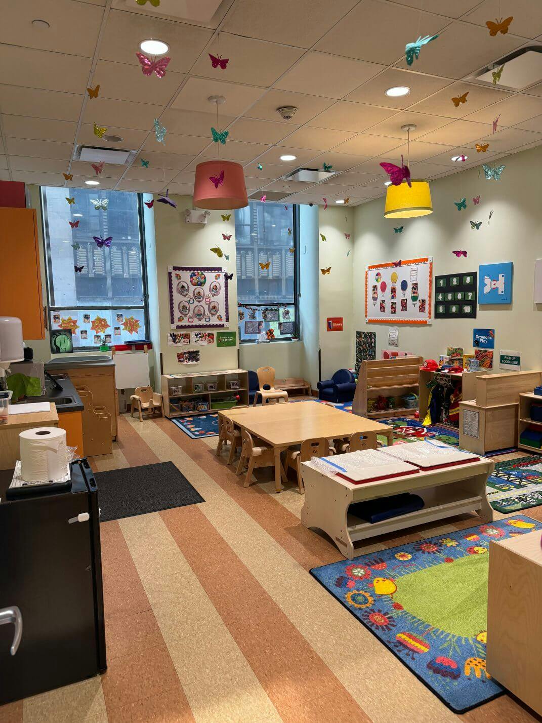 An empty early childhood classroom with multiple small tables, chairs, and play areas