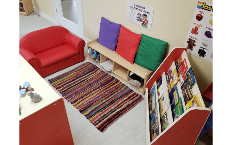 Children's reading area with small red couch, rug, and book display