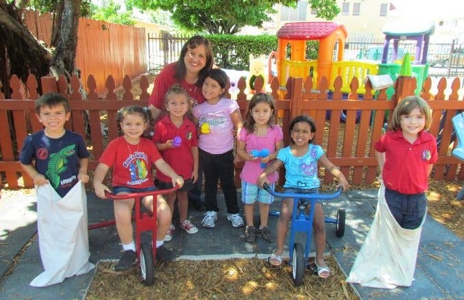 Adult and children posing outdoors, two children in sacks, two on tricycles