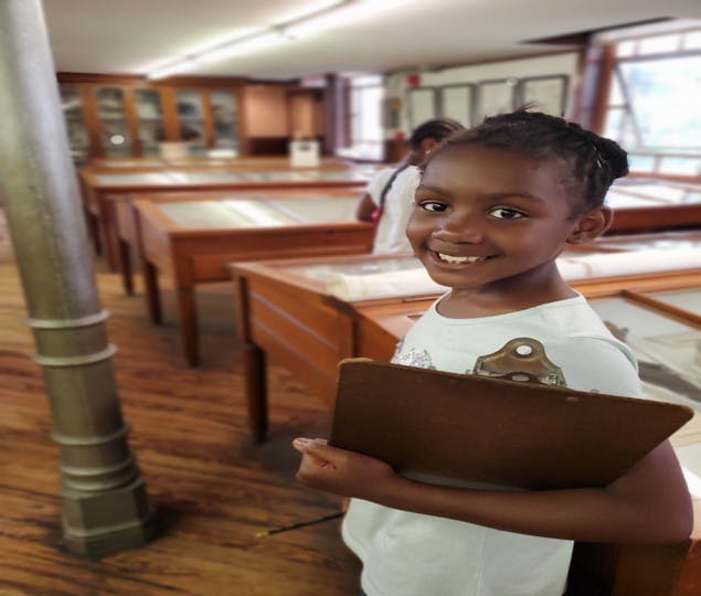 Child holding a clipboard in a room with display cases