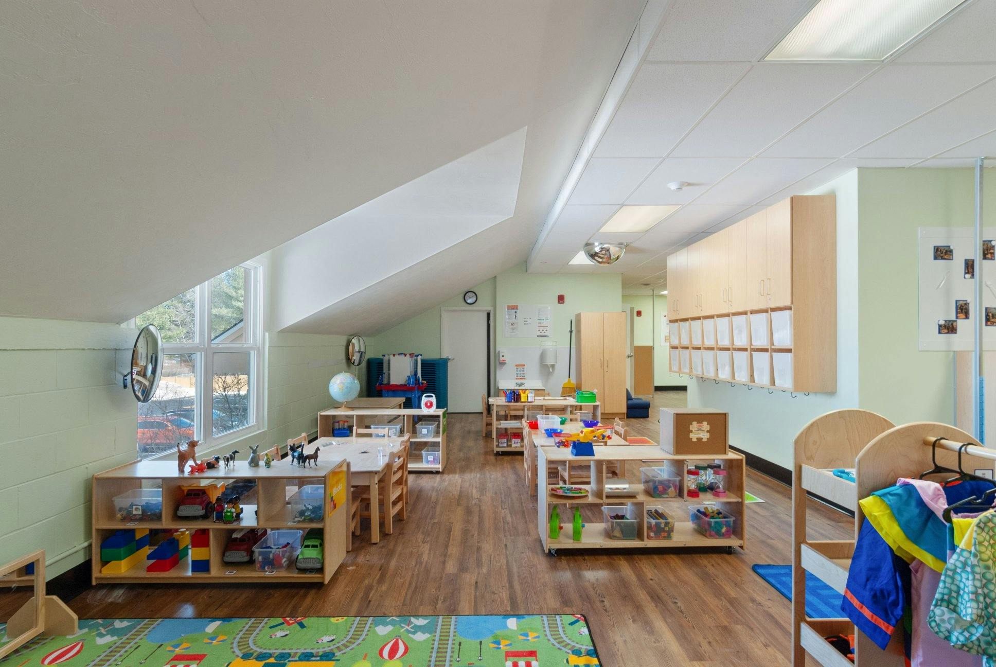 Classroom with tables, shelves of toys, and cubbies under an angled ceiling