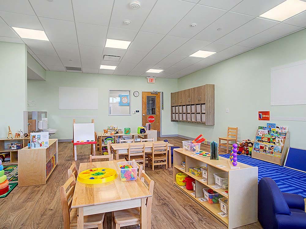 An empty classroom with small wooden tables and chairs, toys, and learning materials