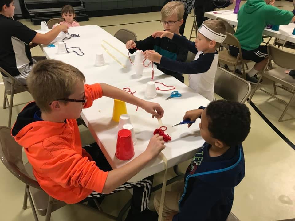 Children at a table doing crafts with cups and string