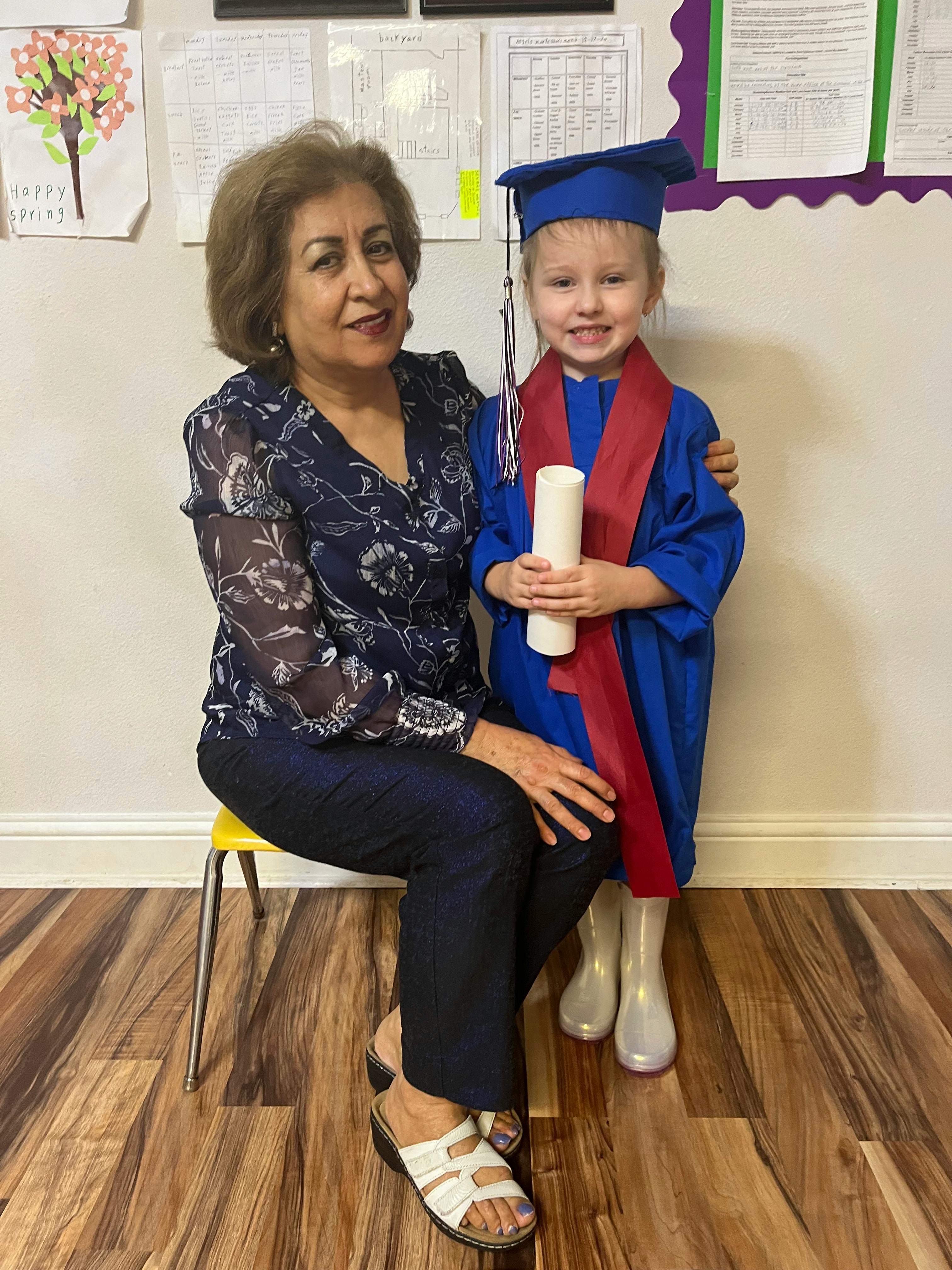Person sitting next to a child in a graduation cap and gown holding a diploma