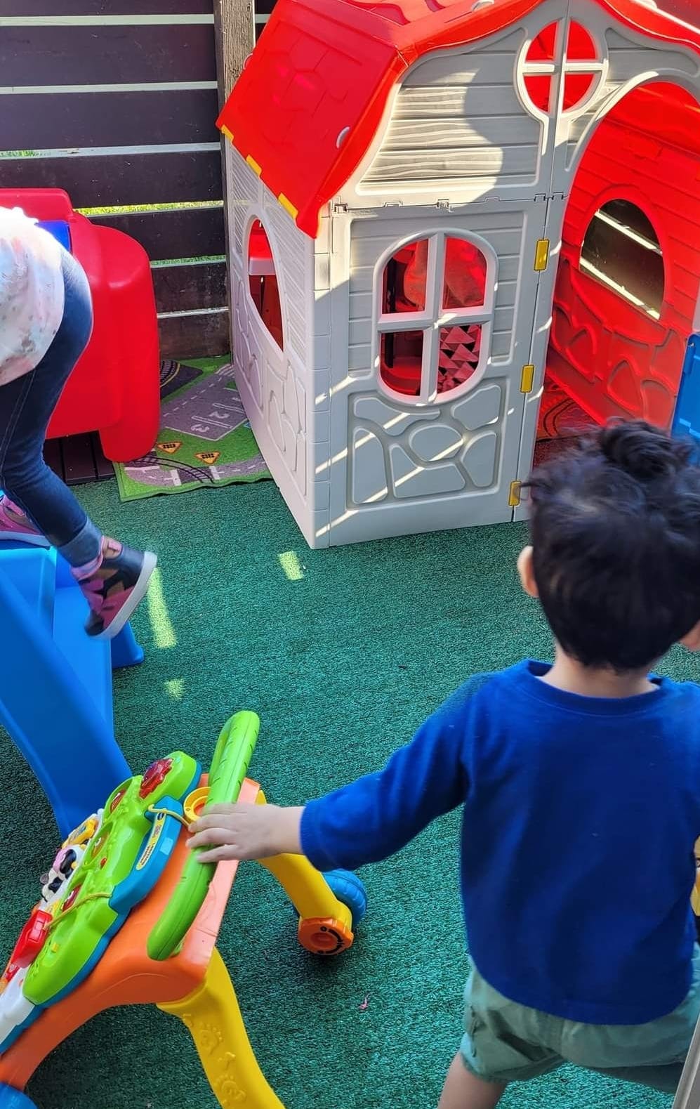 Children playing with a plastic playhouse and toys on artificial turf