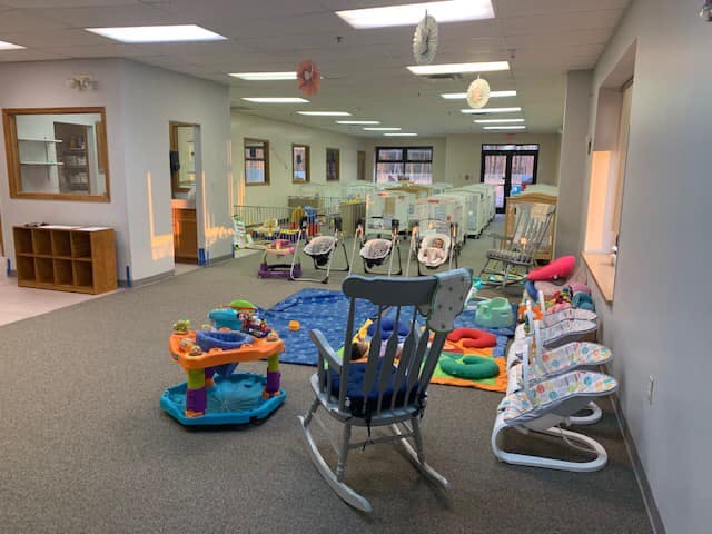 Daycare room with various baby swings, bouncers, and play mats