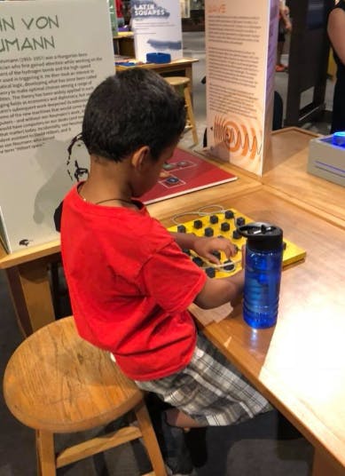 Child in red shirt playing with a yellow board with black buttons
