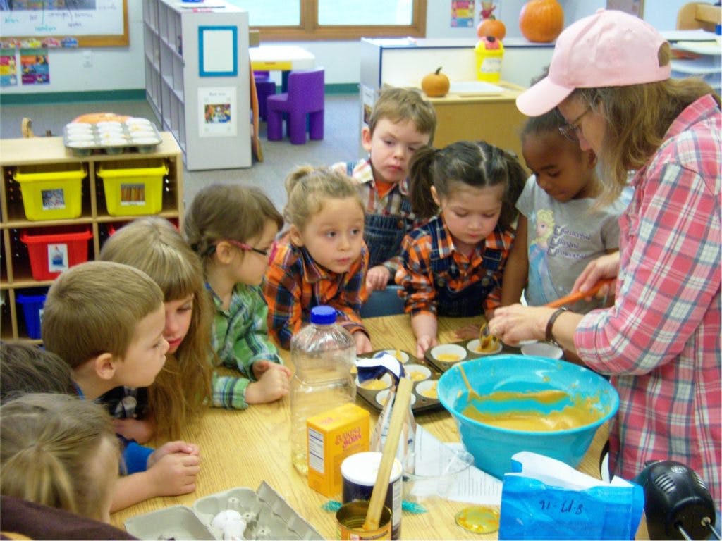 Adult and children gathered around a table, preparing food in a classroom