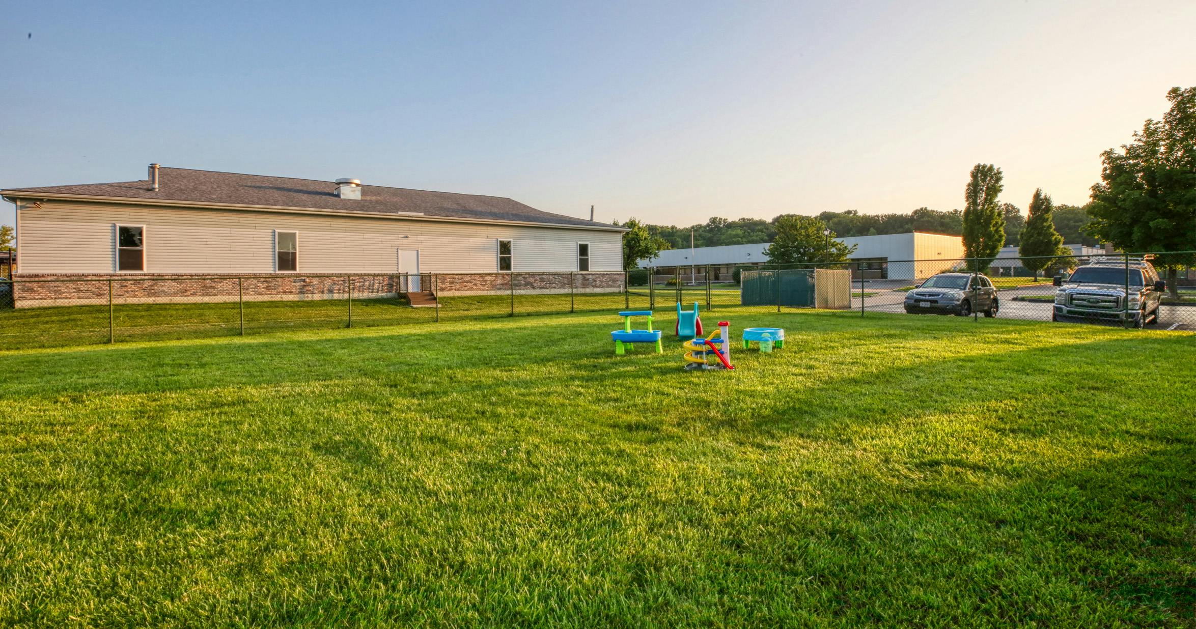 A fenced-in grassy yard with children's toys and a building in the background